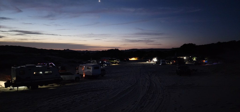 Vehicles parked in a campground at night with a single star in the sky.