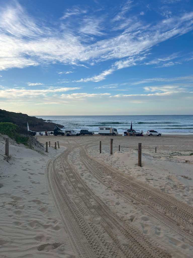 Vehicles parked on the beach with surf in the background.